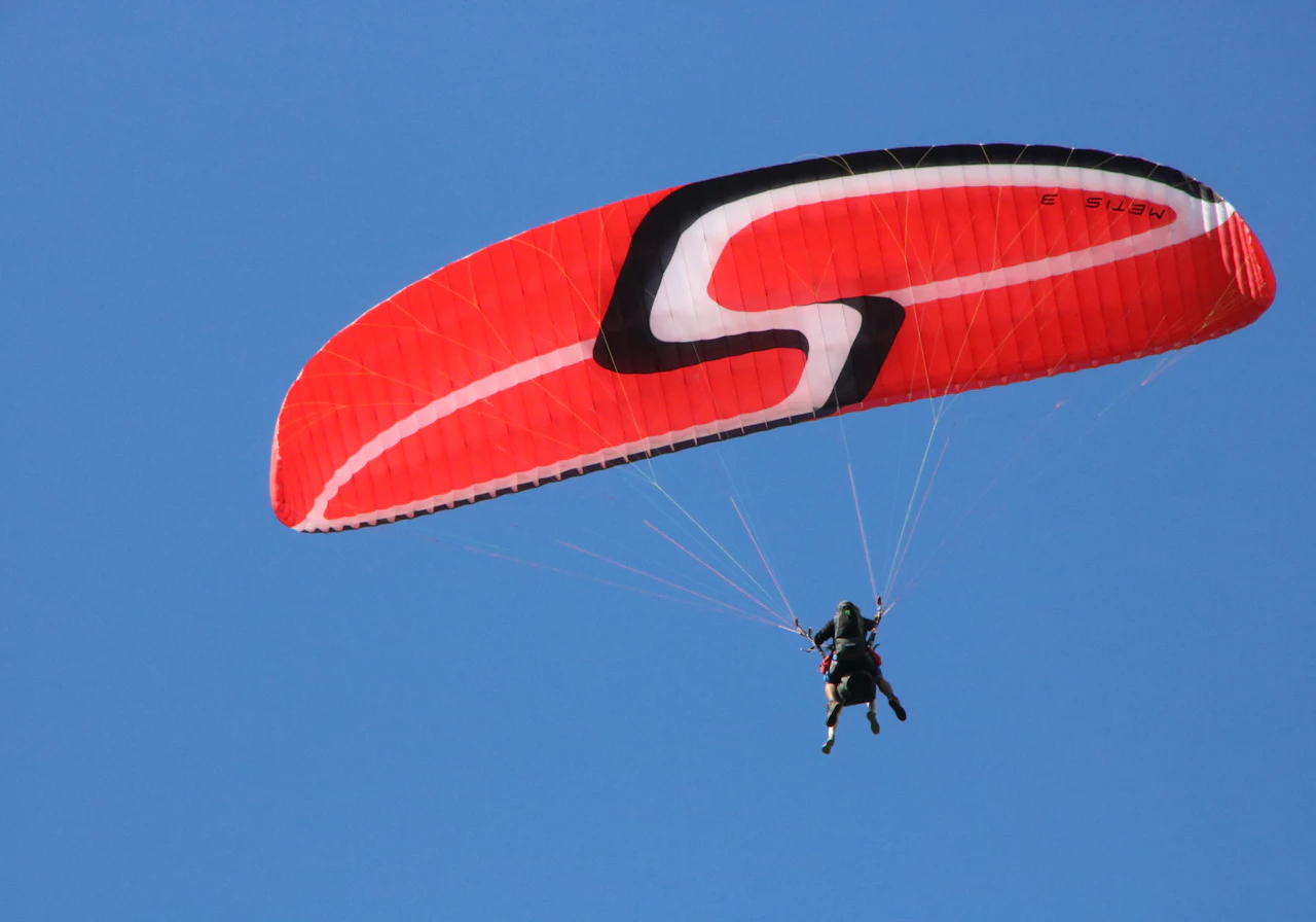 Illustrative paraglider beneath a red canopy in a blue sky